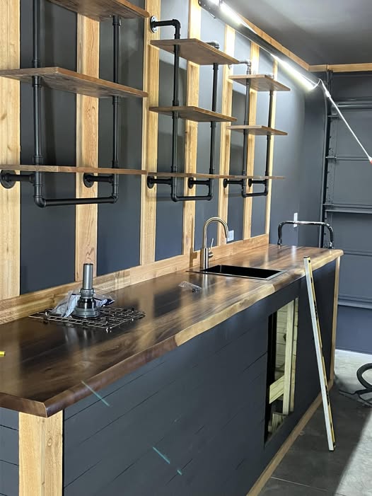 Live-edge walnut bar with a custom sink cutout and black pipe shelving wall, built by Rust & Sawdust in Somerset, KY